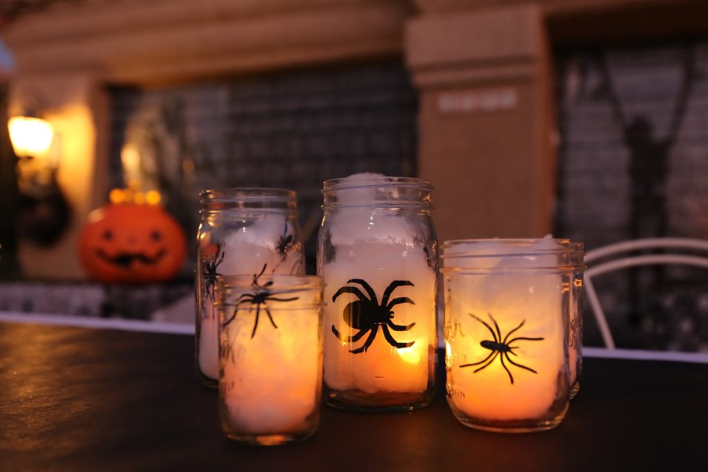 Handmade decorative Halloween mason jars filled with lights, spiders, and spider webs.